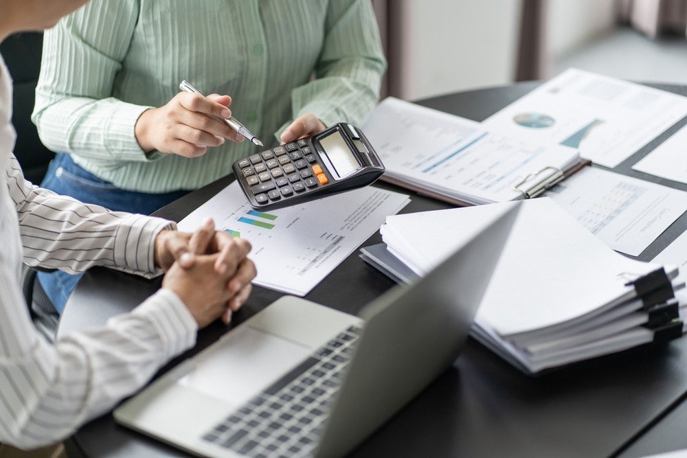 Two people holding a calculator with paperwork in the background