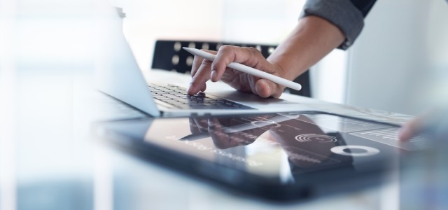 Businessman working on laptop, using mobile phone at modern office.