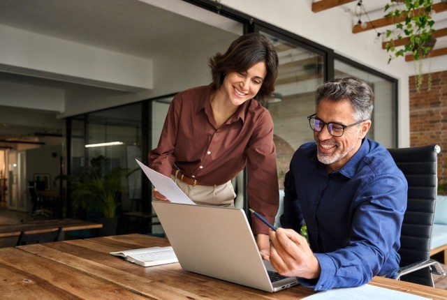 Two people reviewing a document next to a laptop