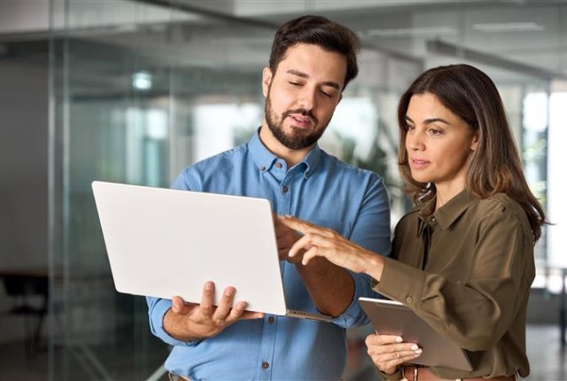 Two people in business clothing holding and pointing to a laptop screen