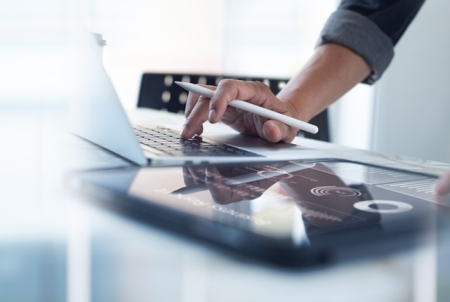 Person typing on a laptop with a tablet next to them