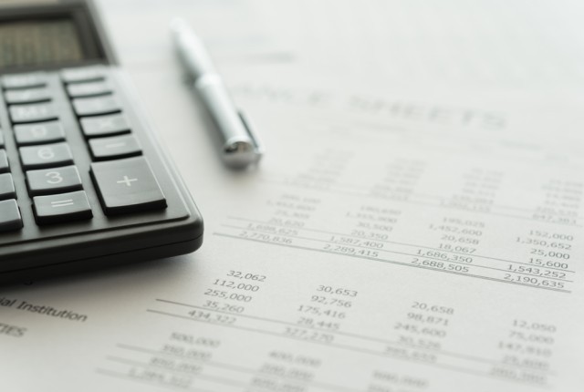A balance sheet with a calculator and a pen sat on top